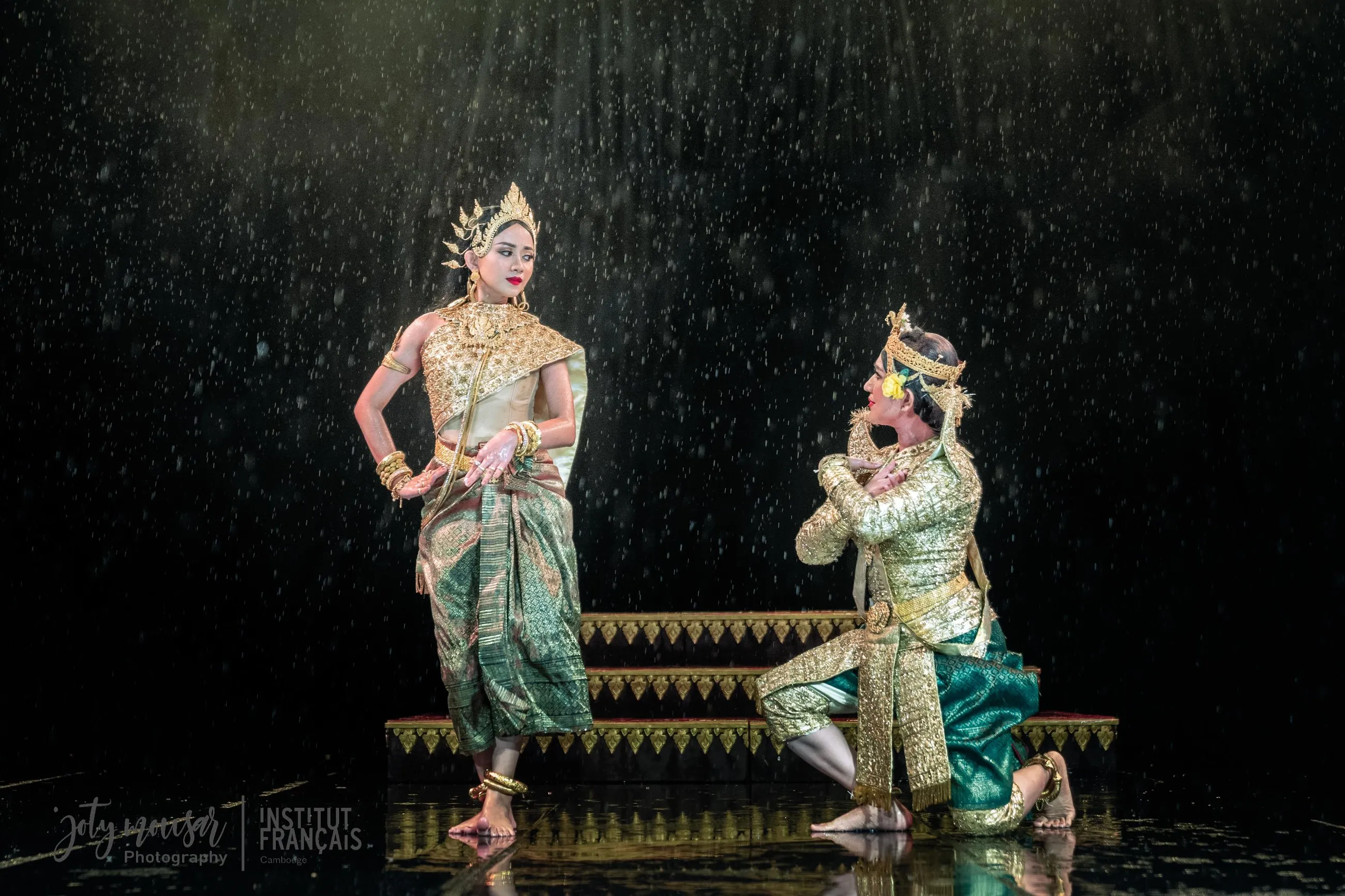 Two Cambodian classical dancers performing together on a rain-soaked stage