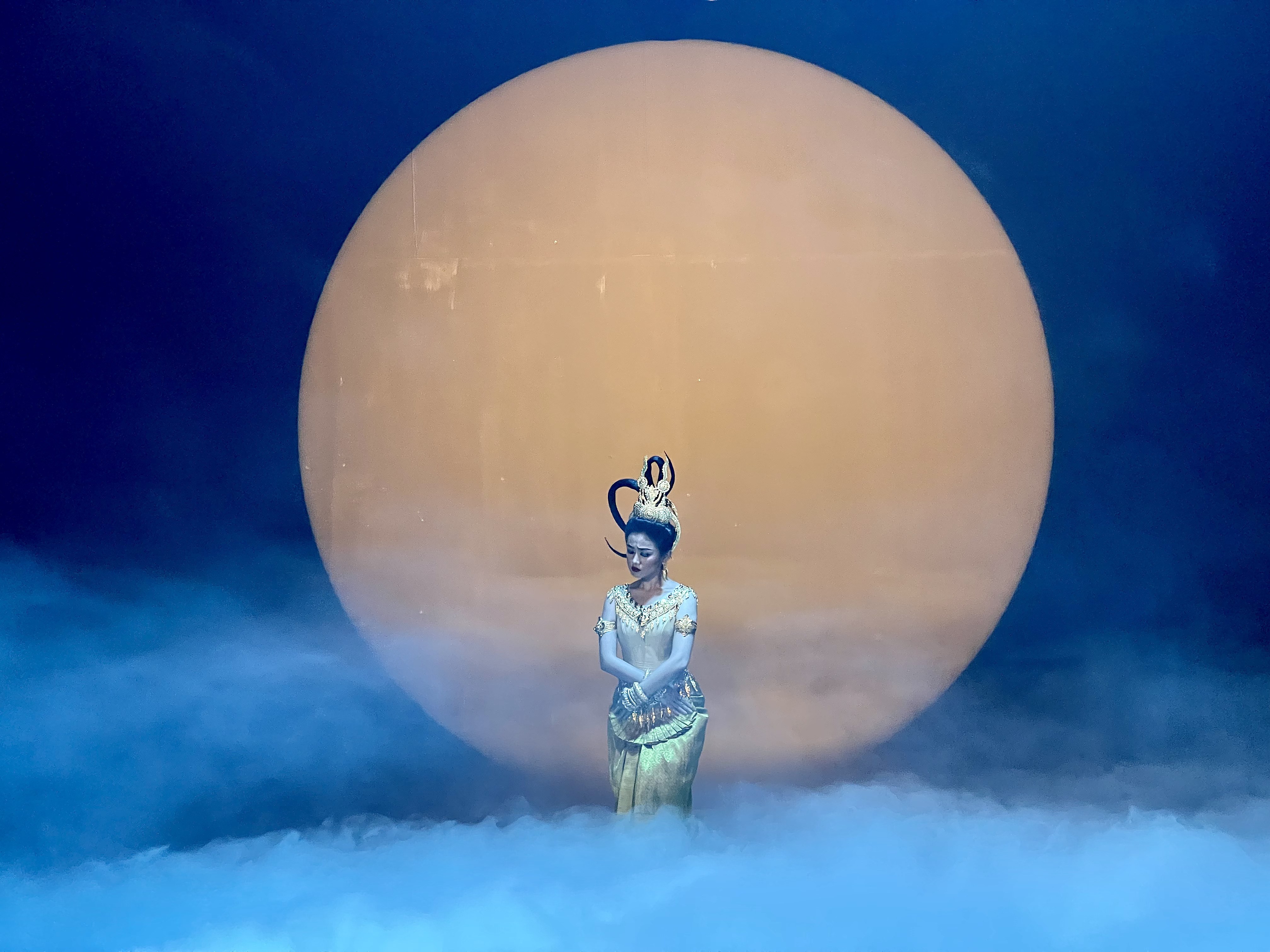 A single dancer before a great moon on a misted stage