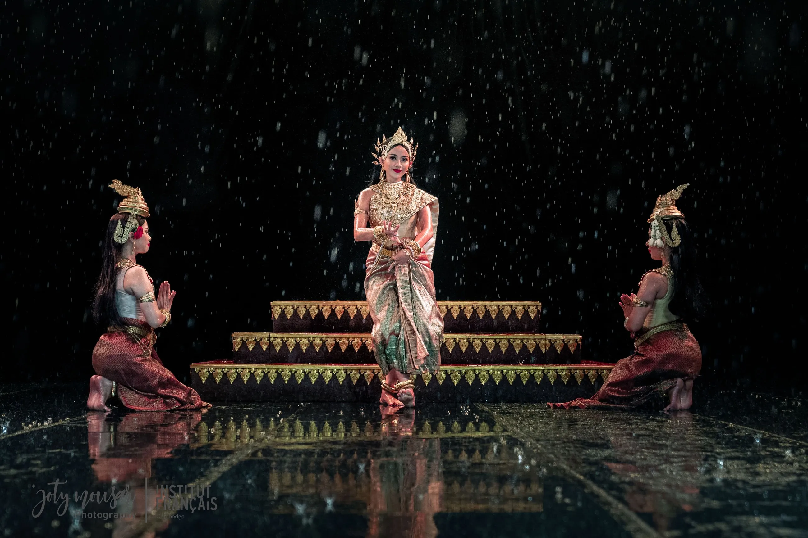 Serei Van Kosaun on a rain-soaked stage, flanked by two kneeling dancers