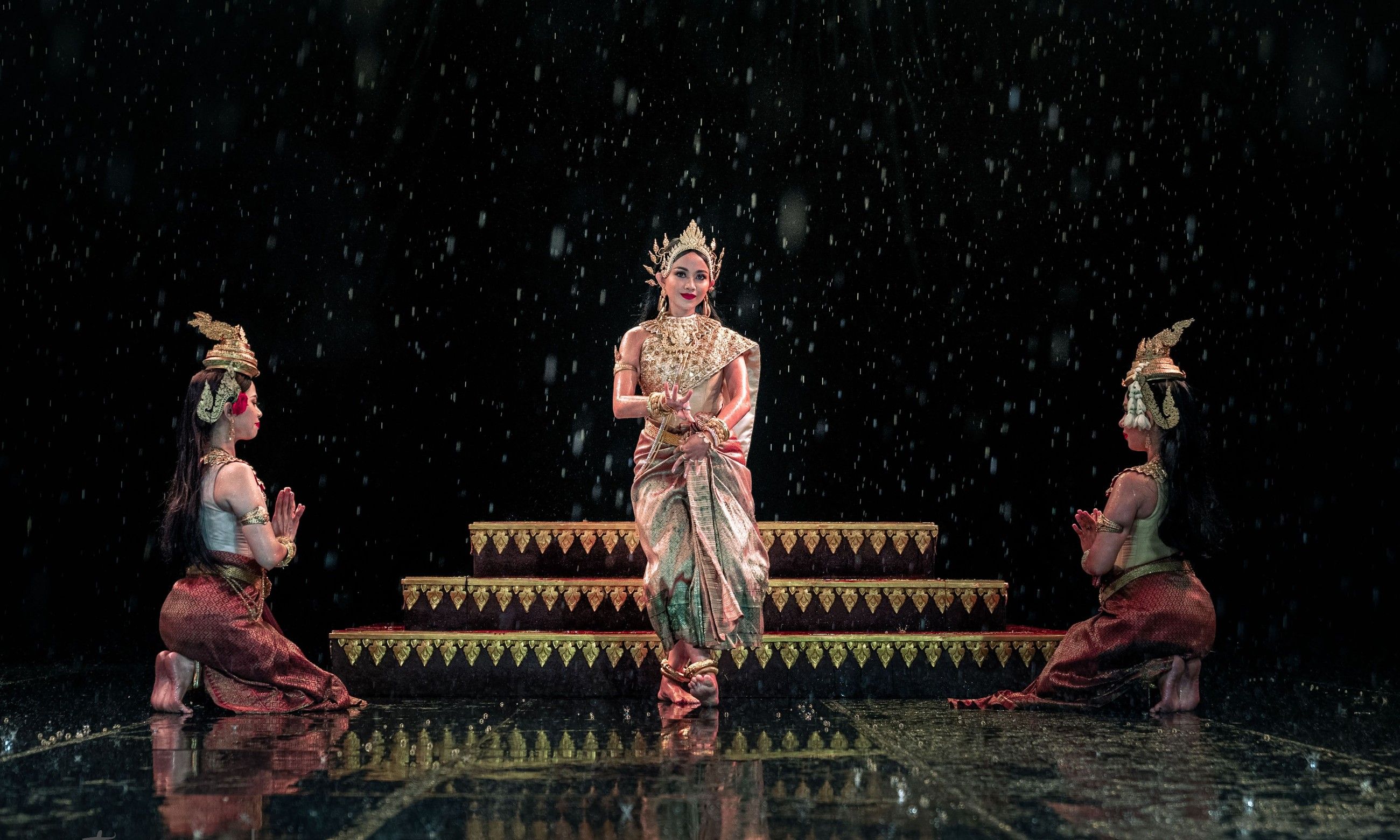 Serei Van Kosaun on a rain-soaked stage, flanked by two kneeling dancers