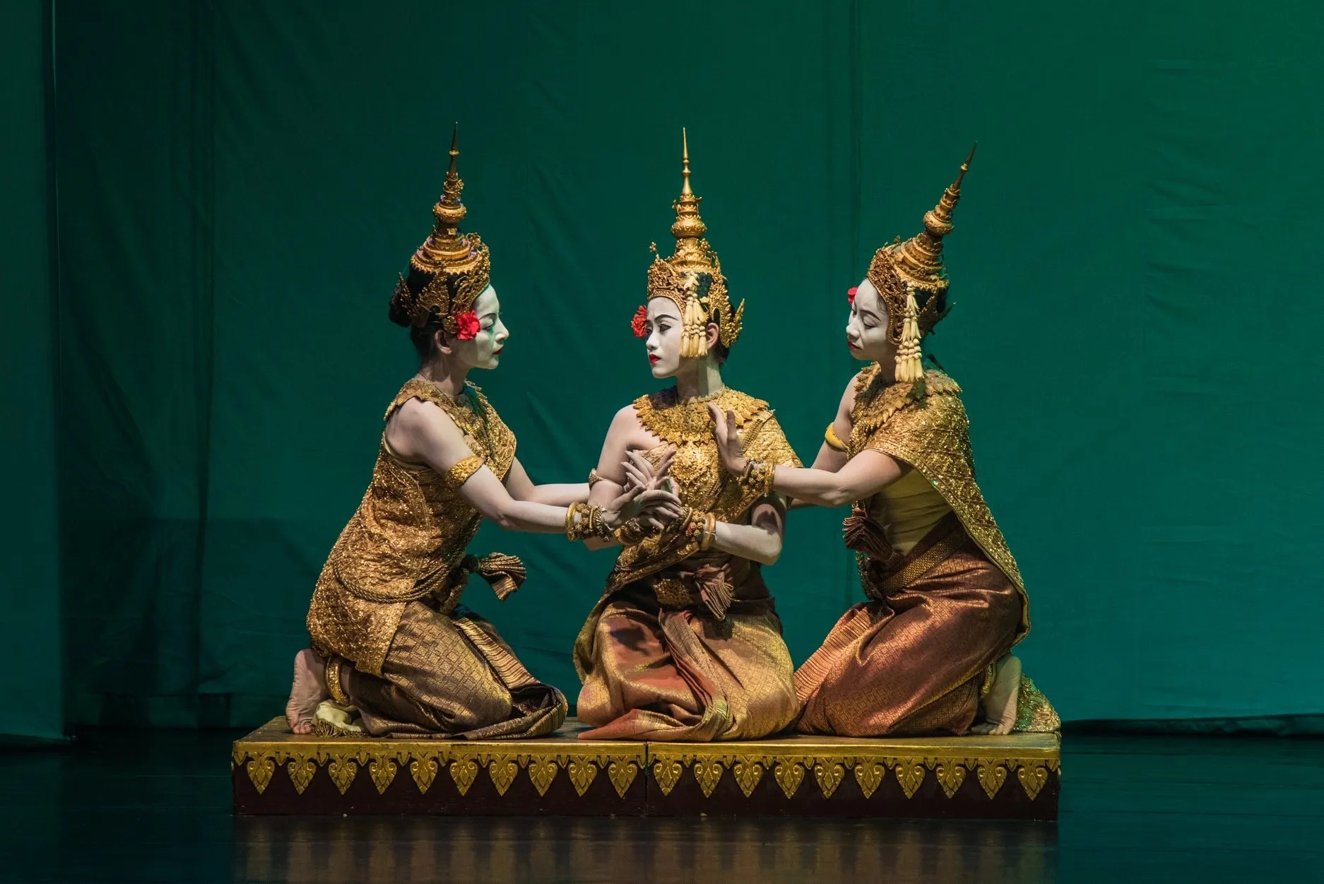 Three Cambodian classical dancers in costume on a green-lit stage
